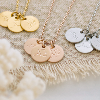 Flat-lay of three-coin Happiness Necklace featuring Arabic calligraphy for patience, gratitude, and reliance on Allah.