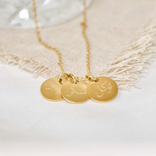 Close-up of three coins on the Happiness Necklace, showcasing Tawakkul (trust in God), Sabr (patience), and Shukr (gratitude) in Arabic calligraphy.